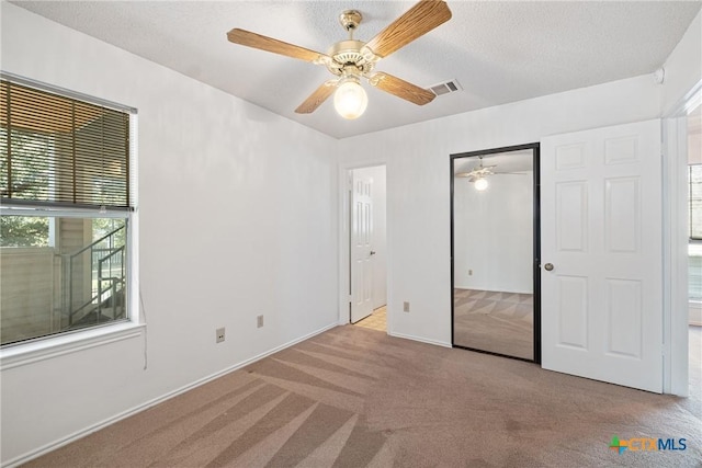 unfurnished bedroom with visible vents, light colored carpet, ceiling fan, a textured ceiling, and a closet