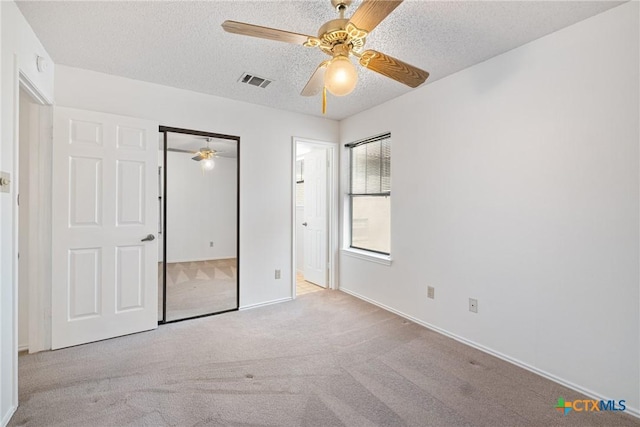 unfurnished bedroom featuring light carpet, visible vents, a ceiling fan, a textured ceiling, and a closet