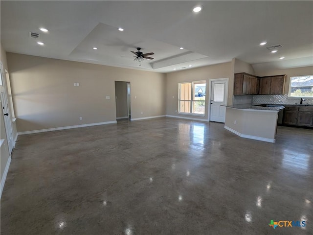 unfurnished living room featuring sink, ceiling fan, a wealth of natural light, and a tray ceiling