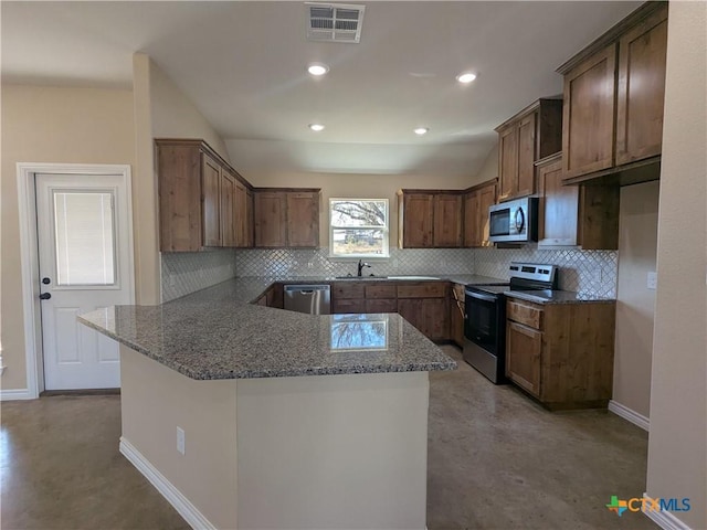 kitchen with kitchen peninsula, light stone countertops, backsplash, appliances with stainless steel finishes, and sink