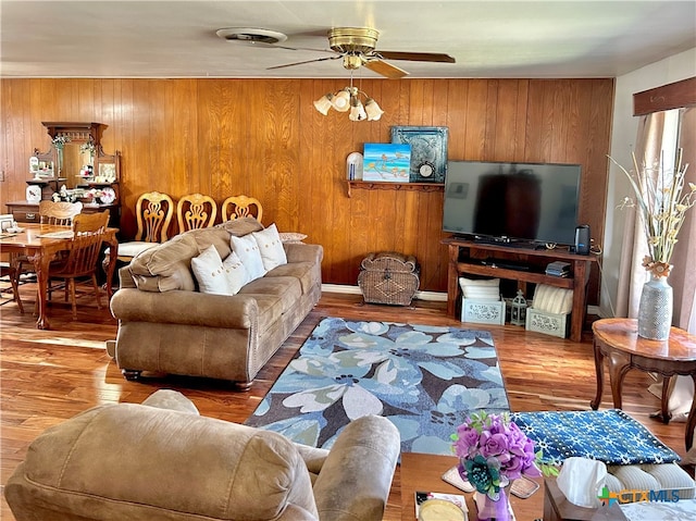 living room with hardwood / wood-style flooring, ceiling fan, and wood walls