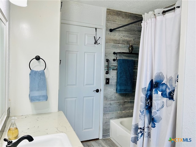 bathroom with hardwood / wood-style floors, wood walls, sink, shower / bathtub combination with curtain, and a textured ceiling