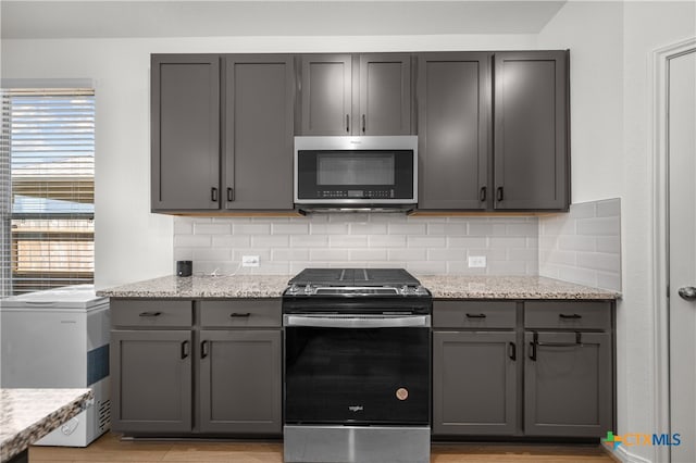 kitchen featuring gray cabinetry, appliances with stainless steel finishes, and light stone counters