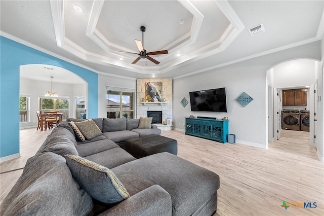 living room featuring washing machine and clothes dryer, ceiling fan, light hardwood / wood-style flooring, a tray ceiling, and ornamental molding