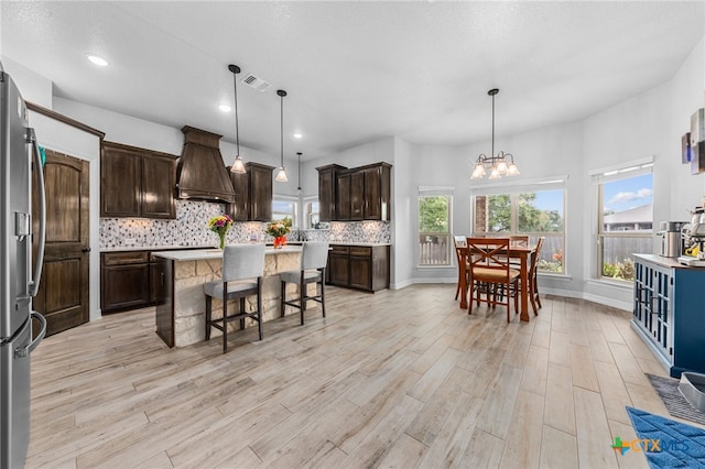 kitchen with dark brown cabinetry, a kitchen island, pendant lighting, and custom range hood