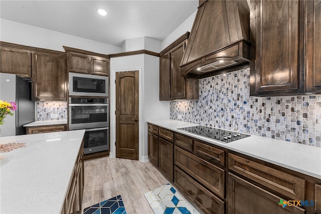 kitchen featuring decorative backsplash, appliances with stainless steel finishes, custom range hood, dark brown cabinets, and light hardwood / wood-style flooring