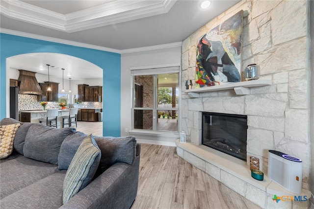 living room featuring a stone fireplace, light hardwood / wood-style flooring, a healthy amount of sunlight, and crown molding