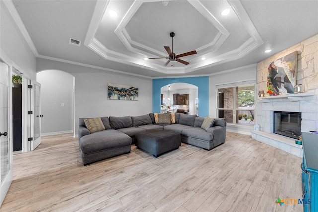 living room with ceiling fan, light hardwood / wood-style floors, a stone fireplace, and ornamental molding