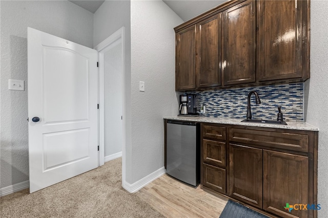 bar with light wood-type flooring, backsplash, stainless steel dishwasher, dark brown cabinetry, and sink