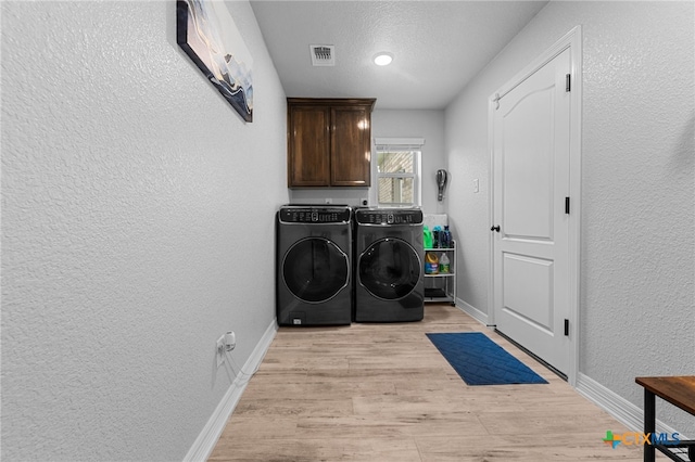 washroom featuring light hardwood / wood-style flooring, cabinets, a textured ceiling, and independent washer and dryer