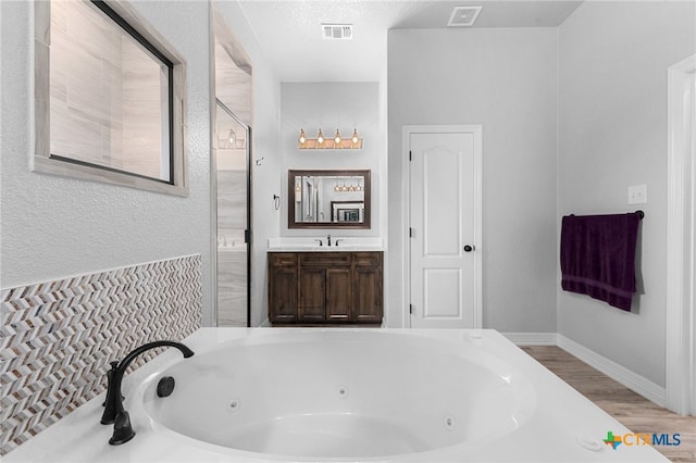 bathroom with hardwood / wood-style floors, vanity, a tub to relax in, and a textured ceiling