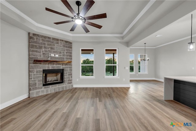 113 Cobblestone Ln, Burnet, TX 78611 - unfurnished living room featuring a tray ceiling, a stone fireplace, wood finished floors, ornamental molding, and ceiling fan with notable chandelier
