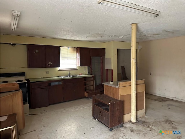 kitchen featuring a textured ceiling, a sink, dark brown cabinets, a center island, and light floors