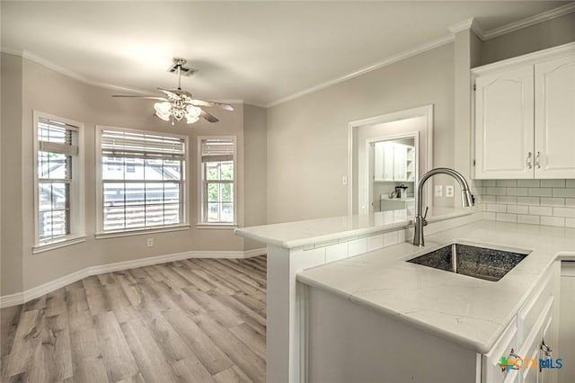 kitchen with kitchen peninsula, light wood-type flooring, backsplash, sink, and white cabinets