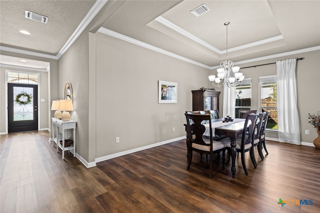 dining area featuring dark hardwood / wood-style flooring, ornamental molding, a textured ceiling, a tray ceiling, and a chandelier