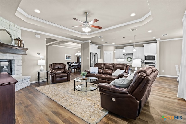 living room with ceiling fan with notable chandelier, dark hardwood / wood-style flooring, a raised ceiling, and crown molding