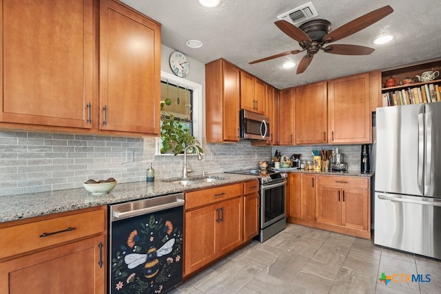 kitchen with tasteful backsplash, light stone counters, stainless steel appliances, ceiling fan, and sink