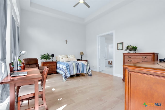 bedroom featuring ceiling fan, connected bathroom, a raised ceiling, and multiple windows