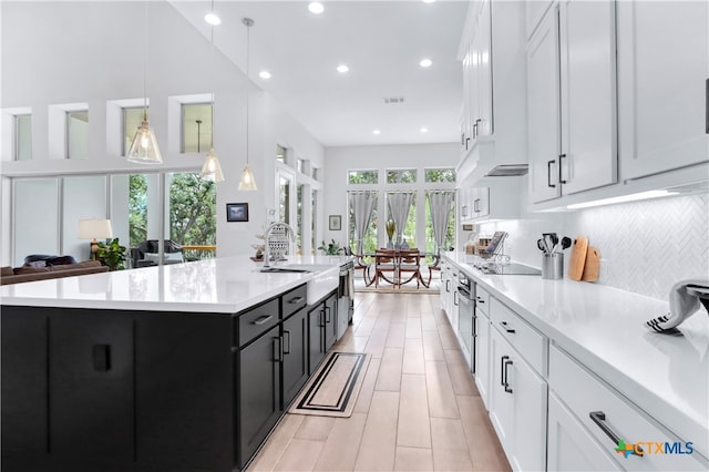 kitchen featuring white cabinetry, hanging light fixtures, an island with sink, and a healthy amount of sunlight