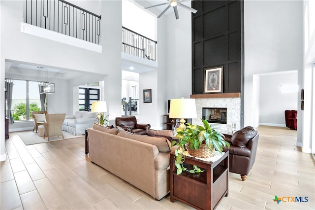 living room featuring a stone fireplace, ceiling fan with notable chandelier, and a high ceiling