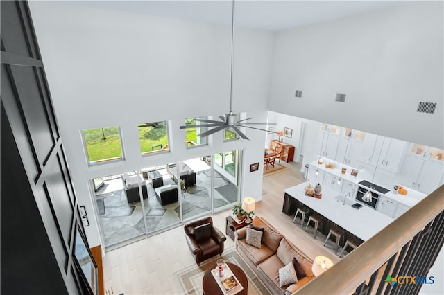 living room with a high ceiling, light wood-type flooring, and ceiling fan