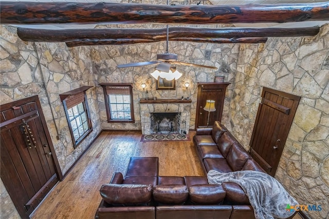 959 Highland Dr, Bandera, TX 78003 - living area featuring a stone fireplace, beamed ceiling, ceiling fan, and hardwood / wood-style flooring