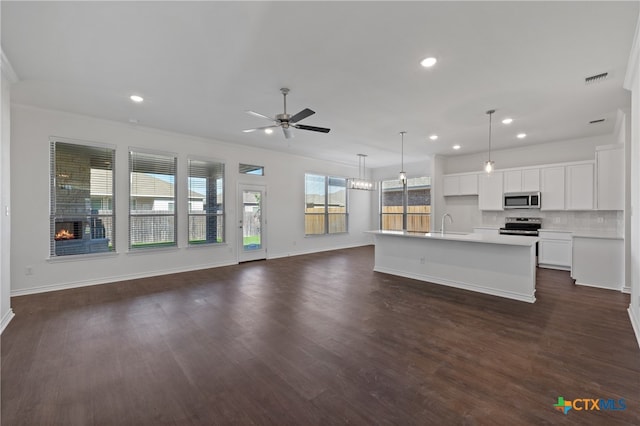 kitchen featuring appliances with stainless steel finishes, decorative light fixtures, white cabinets, dark hardwood / wood-style floors, and an island with sink