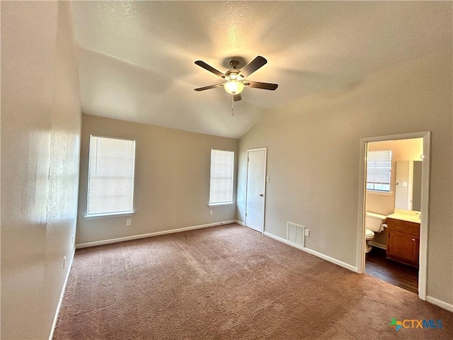 unfurnished bedroom featuring connected bathroom, dark carpet, multiple windows, and lofted ceiling