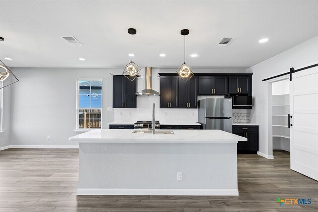 9923 Loma Alta Cir, Converse, TX 78109 - kitchen featuring wall chimney range hood, freestanding refrigerator, a barn door, decorative backsplash, and dark cabinetry