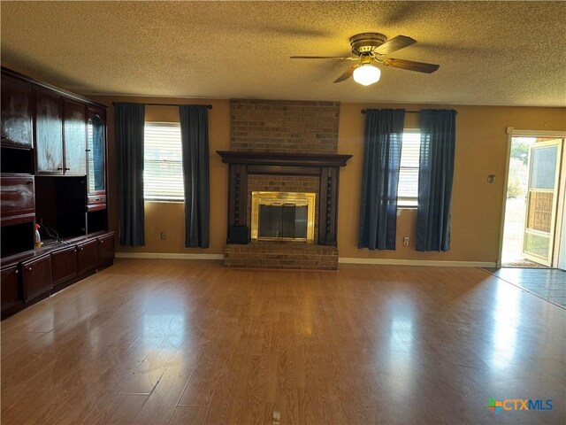 unfurnished living room with wood finished floors, a ceiling fan, baseboards, and a textured ceiling