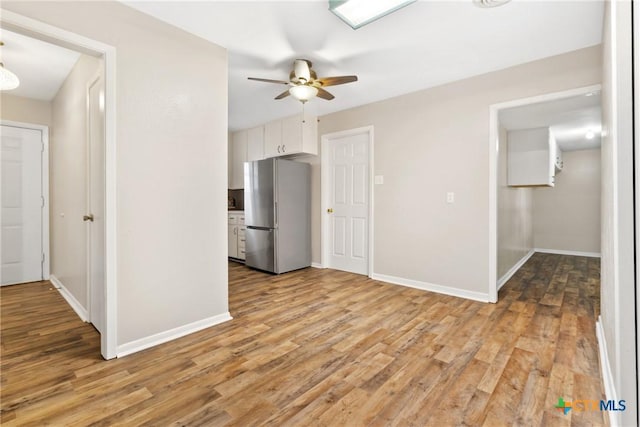 kitchen with baseboards, light wood finished floors, freestanding refrigerator, and white cabinetry