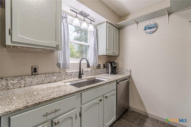 kitchen with white cabinetry, sink, light stone counters, stainless steel dishwasher, and a textured ceiling