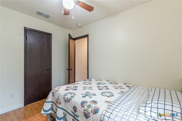 bedroom with ceiling fan, wood-type flooring, and a textured ceiling