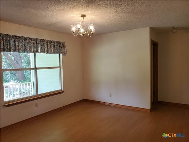 empty room with a textured ceiling, hardwood / wood-style flooring, and an inviting chandelier