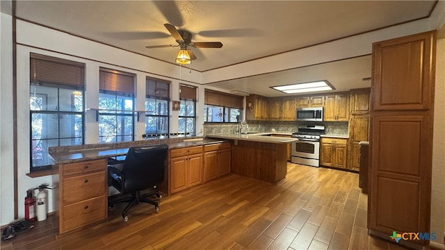 kitchen with ceiling fan, stainless steel appliances, tasteful backsplash, kitchen peninsula, and hardwood / wood-style floors