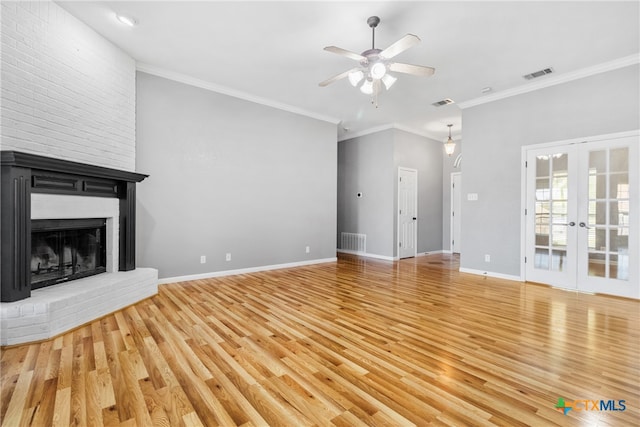 unfurnished living room with french doors, light wood-type flooring, ceiling fan, crown molding, and a fireplace