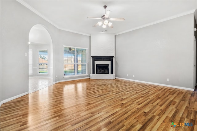 unfurnished living room featuring light wood-type flooring, a brick fireplace, ceiling fan, and ornamental molding