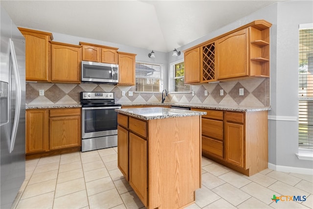 kitchen featuring light tile patterned flooring, backsplash, a kitchen island, light stone counters, and stainless steel appliances