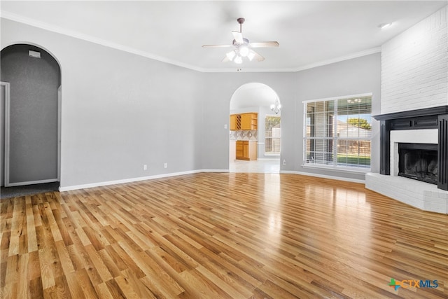 unfurnished living room with ceiling fan with notable chandelier, light wood-type flooring, crown molding, and a brick fireplace