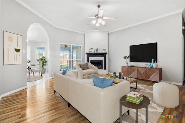 living room featuring a fireplace, crown molding, light hardwood / wood-style flooring, and ceiling fan