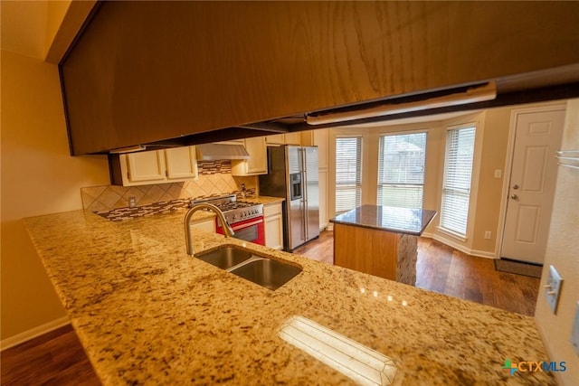 kitchen with hardwood / wood-style floors, sink, appliances with stainless steel finishes, tasteful backsplash, and kitchen peninsula