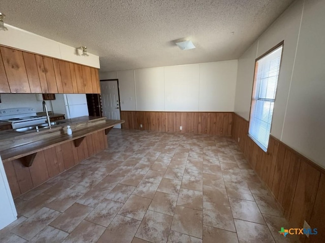 kitchen with a wainscoted wall, white appliances, a textured ceiling, and a kitchen breakfast bar