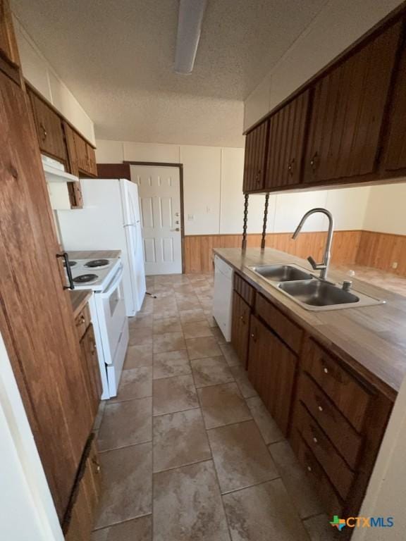 kitchen featuring white appliances, wainscoting, a textured ceiling, under cabinet range hood, and a sink