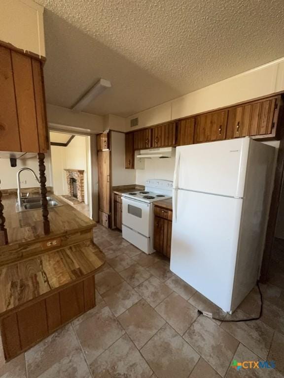 kitchen with white appliances, a fireplace with raised hearth, a textured ceiling, under cabinet range hood, and a sink