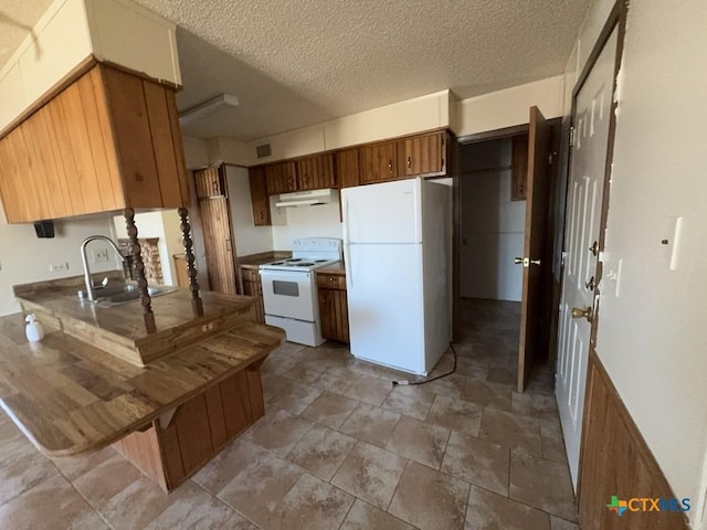 kitchen with white appliances, brown cabinets, a textured ceiling, under cabinet range hood, and a sink