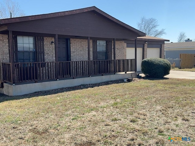 view of front facade with a garage, covered porch, a front yard, and brick siding