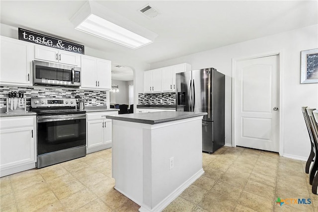 kitchen featuring arched walkways, stainless steel appliances, white cabinets, backsplash, and a center island