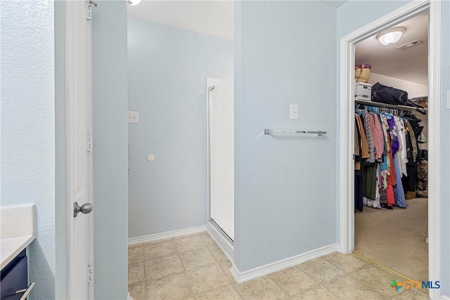 full bathroom with a walk in closet, a stall shower, visible vents, and baseboards