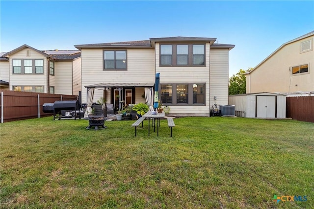 back of house featuring an outdoor fire pit, an outdoor structure, a fenced backyard, a storage shed, and a lawn