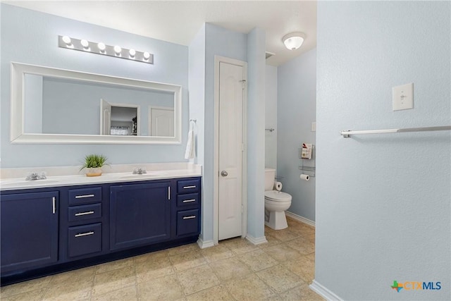 bathroom with baseboards, double vanity, a closet, and a sink